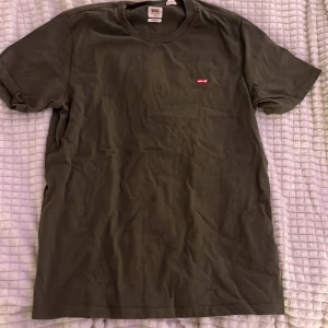 Olivgrön t-shirt från Levi's - Säljer en olivgrön t-shirt från Levi's i storlek M. Klassisk modell med rund halsringning, korta ärmar och liten röd Levi's-logga på bröstet. Skön bomullskvalitet och normal passform, perfekt till jeans eller shorts.