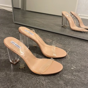 Beige klackar med transparent rem - Snygga beige klackar från Cape Robbin (köpta på Chiquelle) med transparenta remmar och cool genomskinlig klack. Öppen tå och stilren design som ger en modern vibe. Perfekta för dig som vill sticka ut med en trendig look. (Aldrig använda)