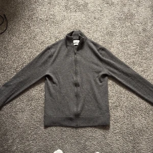 Grå merinoullskofta från These Glory Days - Snygg grå kofta i merinoull från These Glory Days. Klassisk modell med hel dragkedja framtill och hög krage. Perfekt för lager-på-lager och funkar året runt. Mjuk och stilren, passar till allt. Storlek M men sitter mer som S. Nypris 1400kr