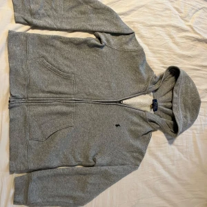 Grå hoodie från Polo Ralph Lauren - Säljer en grå hoodie från Polo Ralph Lauren med dragkedja och huva. Tröjan har två stora fickor fram och den klassiska broderade Polo-loggan på bröstet. Tillverkad i mjuk bomullsmix. Tveka inte att fråga om ni vill ha fler bilder eller undrar något, Mvh Olle