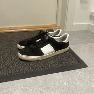 Valentino flycrew 44 - Snygga sneakers i svart mocka och vitt skinn med klassisk låg profil och vit sula. Skorna har svart snörning och en stilren design med vit panel på sidan. Perfekta för dig som gillar en clean och tidlös look.