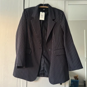 Randig kavaj från Bik Bok - Snygg mörkblå kavaj från Bik Bok i storlek XS/S med vita smala ränder. Klassisk passform med krage, knappstängning och två fickor framtill. Perfekt för dig som gillar stilrena och trendiga plagg med lite edge. Helt ny med prislapp