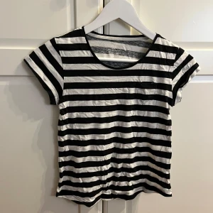 Randig t-shirt från H&M - Säljer en svartvit randig t-shirt från H&M i ekologisk bomull. Den har en liten bröstficka och korta ärmar. Perfekt för en avslappnad stil. 🖤🤍