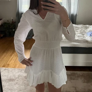 Vit klänning med volangdetaljer - Säljer en söt vit klänning med volangdetaljer och v-ringad hals. Klänningen har långa ärmar och en smickrande passform med resår i midjan.🤍Använd endast en gång, och säljer för att den inte kommer till användning längre.