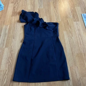 Svart one-shoulder klänning från H&M - Snygg svart one-shoulder klänning från H&M med volangdetalj vid axeln. Perfekt för en kväll ute eller en speciell tillställning. Klänningen har en elegant och stilren design som framhäver figuren.