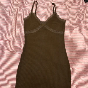 Brun ribbad klänning från Divided - Säljer en brun ribbad klänning från Divided med spetsdetaljer vid bysten och justerbara axelband. Perfekt för en stilren look. Klänningen är figurnära och bekväm att bära.