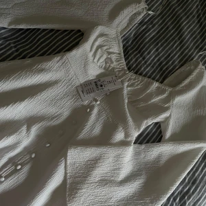 Vit klänning med knappar - Säljer en söt vit klänning med knappar framtill och långa ärmar. Klänningen har en lätt textur och en smickrande passform. Perfekt för sommarens alla tillfällen och studenten!! 😍