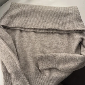 Beige stickad tröja från H&M - Mysig beige stickad tröja från H&M med en bred krage som kan vikas ner. Perfekt för kyliga dagar med sin mjuka och bekväma passform. Tröjan har långa ärmar och ribbade detaljer vid krage och ärmslut.