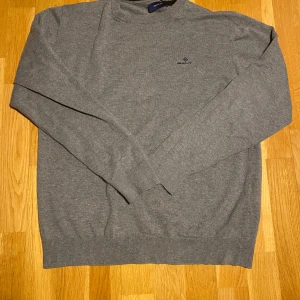 Grå tröja från GANT - Säljer en stilren grå tröja från GANT med broderad logga på bröstet. Tröjan har långa ärmar och ribbade muddar vid ärmslut och nederkant. Perfekt för en avslappnad och snygg look.