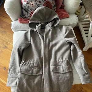 Beige Jacka från John Henric - Säljer en stilren beige Jacka från John Henric. Den har en avtagbar huva och praktiska fickor framtill. Jackan är långärmad och har en dragkedja för enkel stängning. Perfekt för kyligare dagar.