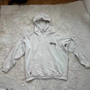 Stussy hoodie - Säljer en beige hoodie från Stussy med design på ryggen och Stussy-logga på bröstet. Hoodien har en klassisk känguruficka och justerbar huva med dragsko. Riktigt skön passform! 