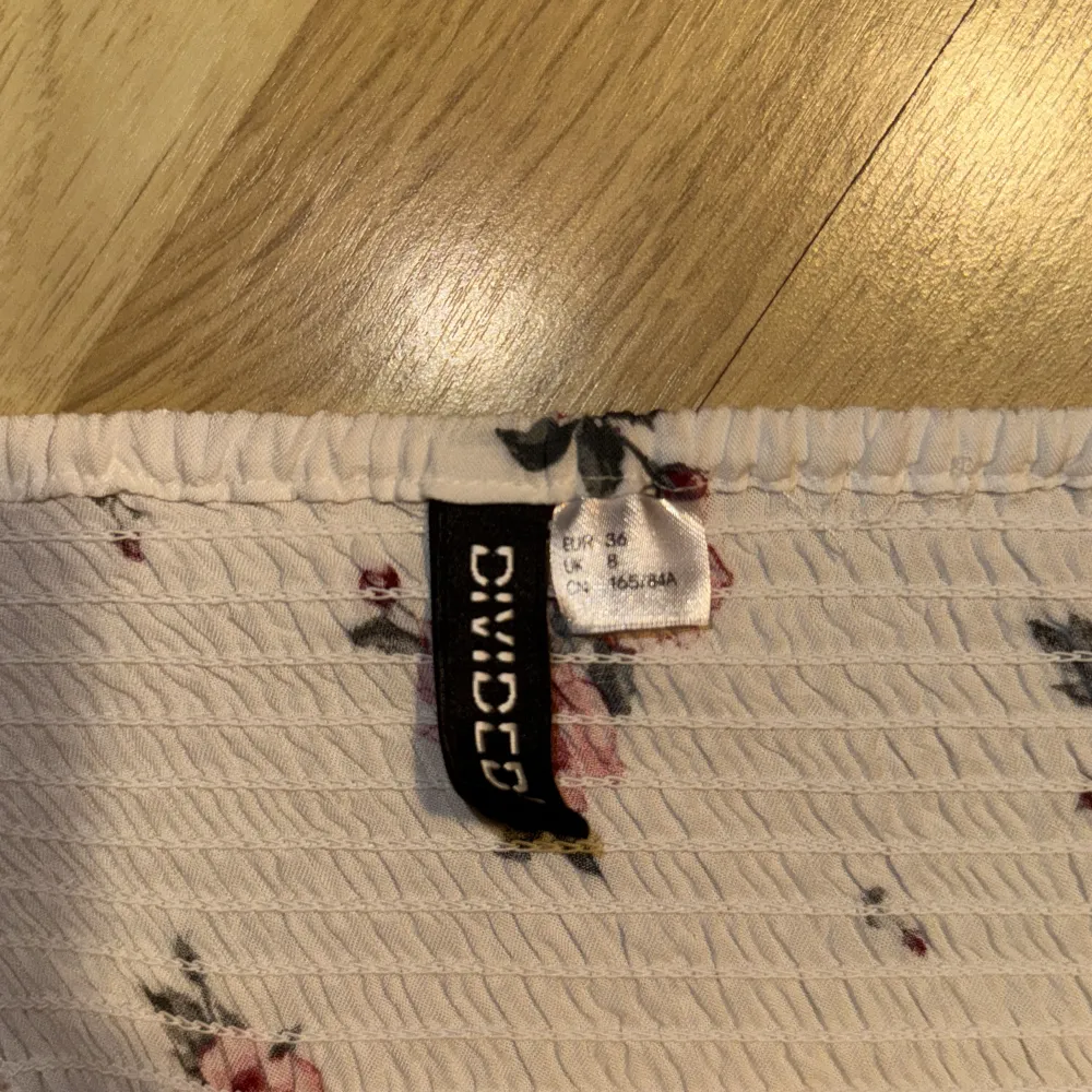 Söt blommig klänning från H&M med rosa rosor på en ljus bakgrund. Klänningen har smala axelband och en avslappnad passform, perfekt för varma dagar. Den är tillverkad i ett lätt och bekvämt material.. Mekot.