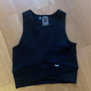Croppad Stronger topp - Säljer denna träningstopp från Stronger 🖤Ribbad med omlott midja i storlek XS, liten i storleken! Använd fåtal gånger, bra skick!