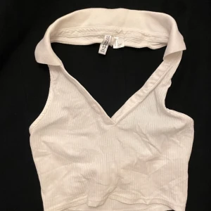 Vit ribbad halterneck topp från H&M - Säljer en stilren vit ribbad halterneck topp från H&M med v-ringning. Perfekt för varma dagar. Toppen har en snygg och enkel design som passar till det mesta.