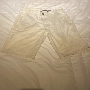 Vita shorts från Tailored Originals - Säljer ett par vita shorts från Tailored Originals. De har en klassisk design med knappar och dragkedja framtill. Perfekta för en avslappnad stil.