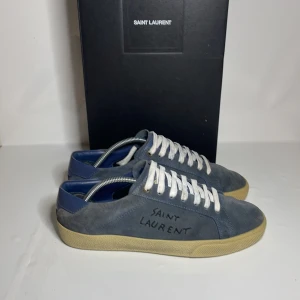 Saint Laurent skor - Snygga blå sneakers från Saint Laurent i mocka med vit snörning och beige sula. Storlek 39,5 men sitter som 40 Perfekta för en stilren look med den ikoniska loggan på sidan.