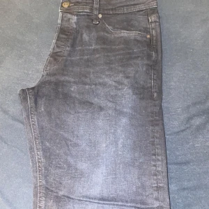 Svarta jeans från Jack & Jones - Snygga svarta jeans från Jack & Jones med en bekväm passform. De har en klassisk design med knapp och dragkedja framtill. Perfekta för en stilren look.