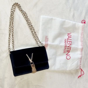 Marinblå axelväska från Valentino - Snygg marinblå axelväska från Valentino med en elegant kedjerem och dekorativ tofsdetalj framtill. Perfekt för att ge din outfit en lyxig touch. Kommer med en praktisk dustbag för förvaring.