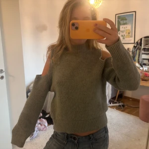 Grön stickad tröja med öppna axlar - Säljer en snygg grön stickad tröja med öppna axlar. Tröjan har långa ärmar och en ribbad design som ger en skön passform. Perfekt för kyligare dagar!