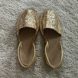 Glittriga guld sandaler - Snygga sandaler i glittrigt guld med öppen tå och rem runt hälen. Perfekta för att lysa upp din outfit med en touch av glamour. Använda max 2 gånger 