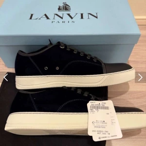 Svarta sneakers från Lanvin - Snygga svarta sneakers från Lanvin med en stilren design. Skorna har en överdel i mocka och en tå i skinn, vilket ger en lyxig känsla. De har svarta snören och en vit sula som kontrasterar snyggt mot det mörka. Perfekta för en trendig look.