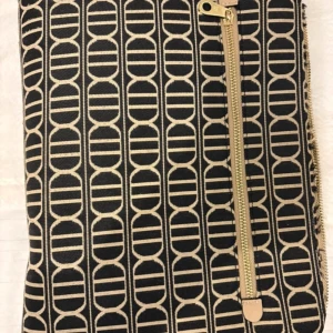 Svart och beige kuvertväska med dragkedja - Snygg kuvertväska i svart och beige med ett unikt geometriskt mönster. Väskan har en praktisk dragkedja i guld som ger en elegant touch. Perfekt för att bära dina nödvändigheter med stil.