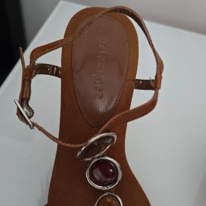 Bruna sandaler Priciples  med klack och dekorativa stenar - Snygga bruna sandaler Principles  med klack och justerbara remmar. Sandalerna har dekorativa stenar i olika färger och en elegant design som passar perfekt för sommarens tillfällen.