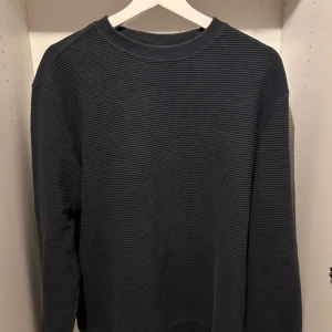 Mörkblå ribbad tröja - Säljer en stilren mörkblå ribbad tröja med rund hals. Tröjan har långa ärmar och en bekväm passform, perfekt för kyligare dagar. Passar bra till både jeans och chinos.