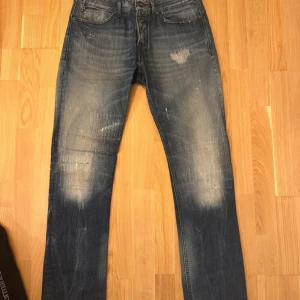 Blå jeansbyxor med slitningar - Snygga blå jeansbyxor med coola slitningar och en klassisk femficksdesign. Perfekta för en avslappnad stil med en touch av edge. De har en straight passform och är tillverkade i slitstarkt denim.