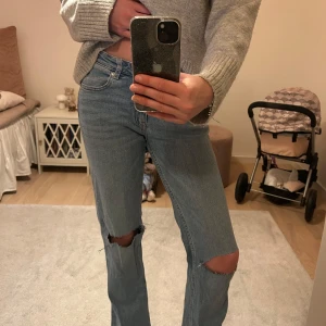 Blå jeans med slitningar - Snygga blå jeans med slitningar på knäna. De har en klassisk femficksdesign och en knappgylf. Perfekta för en avslappnad stil.