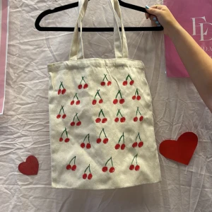 Beige shoppingväska med körsbärsmönster - Vi är ett UF företag som säljer tygväskor med handmålade tryck på framsidan. Perfekt för att bära med sig det nödvändigaste med stil.