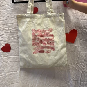 Vit shoppingväska med läppmotiv - Vi är ett UF företag som säljer tygväskor med handmålade tryck på framsidan. Perfekt för att bära med sig det nödvändigaste med stil.