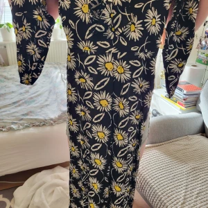 Svart blommig klänning med solrosor. Dress en hel - Snygg svart klänning med ett härligt blommönster av solrosor i gult och vitt. Klänningen har långa ärmar och en figurnära passform som framhäver silhuetten. Perfekt för en somrig look!