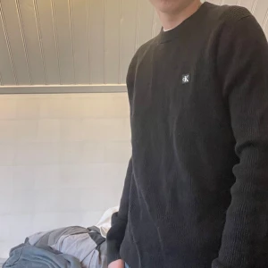 Svart tröja från Calvin Klein Jeans - Säljer en stilren svart tröja från Calvin Klein Jeans. Tröjan har en diskret CK-logga på bröstet och är ribbad för en snygg look. Perfekt för en casual stil. Nypris ca 799. Oanvänd etikett sitter fortfarande kvar med en qr kod. Priset ej hugget i sten. Skriv vid funderingar:)