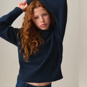 Mörkblå stickad hoodie - Säljer en mysig mörkblå stickad hoodie med långa ärmar. Perfekt för kyliga dagar med sin mjuka och bekväma passform. Den har en klassisk huva och ribbade muddar vid ärmslut och nederkant.