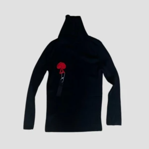 Black Turtleneck With Spade - Snygg svart polotröja med en unik röd spade på bröstet. Tröjan är ribbad och har långa ärmar, perfekt för en stilren look. Passar både till vardags och speciella tillfällen.