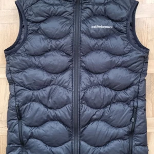 Svart dunväst från Peak Performance - Snygg svart dunväst från Peak Performance modell HELIUM andvänd fåtal gånger då jag inte gillade modellen med quiltad design och dragkedja framtill. Perfekt för kyliga dagar och ger en sportig look. Västen har praktiska fickor med dragkedja.