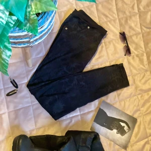 Svarta blommiga leggings - Snygga svarta byxor med ett subtilt blommönster. De har en tight passform och är perfekta för att ge en stilren look. Byxorna har en midwaist design och är tillverkade i ett mjukt material som ger komfort hela dagen!  Har också snygga ”knappar” vid fickorna.  Öppen för prisförslag! 