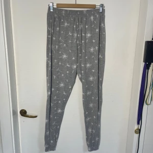 Grå pyjamasbyxor med maskrosmönster - Säljer ett par grå mjukisbyxor från Basic U med ett fint vitt maskrosmönster. Byxorna har en elastisk midja för extra komfort och är perfekta för en avslappnad stil. Något nopprig.