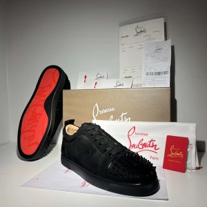 Christian Louboutin - Snygga svarta sneakers från Christian Louboutin med ikoniska röda sulor och nitar på ovansidan. Skorna har snörning och en stilren design som sticker ut. Perfekta för den som vill ha en edgy look.