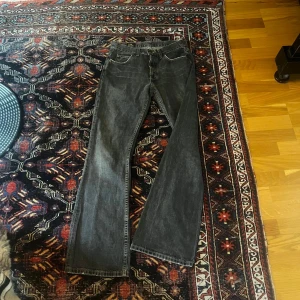 Grå bootcut jeans från Lee - Säljer ett par svarta jeans från Lee med klassisk femficksdesign och snygga kontrastsömmar. Jeansen har bootcut-ben och är tillverkade i slitstarkt denimtyg. Perfekta för dig som gillar en tidlös och avslappnad look.