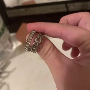 Kedjeformad silverring - Säljer en stilren ring i silverfärgad metall med kedjeinspirerad design. Perfekt för dig som gillar en edgy och trendig look. Ringen har en öppen struktur med tydliga länkar som ger en cool vibe.
