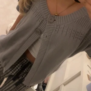 Grå stickad kofta - Säljer en ljusgrå stickad kofta från Andiata med korta ärmar och två stora knappar framtill