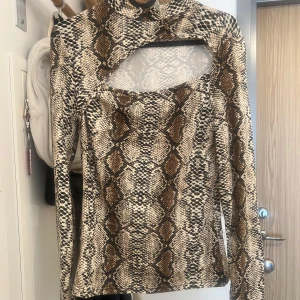 Långärmad topp med ormmönster - Snygg långärmad topp med  ormmönster i beige, brunt och svart. Toppen har en unik cut-out detalj vid halsen och sitter figurnära.