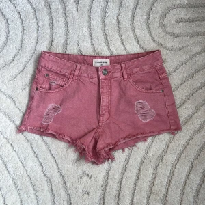 Rosa jeansshorts från Denim Reserved - Snygga rosa jeansshorts från Denim Reserved med slitna detaljer och fransig kant. Klassisk femficksmodell med knapp och dragkedja framtill. 