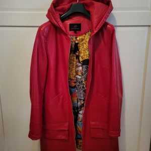 Röd jacka med huva från Angmifer - Snygg röd jacka med huva från Angmifer. Skinnimitation. Jackan har dragkedja framtill, stora fickor och ett färgstarkt, mönstrat innerfoder med mosaik- och grafiska detaljer i gult, blått, orange och svart. Perfekt för dig som vill sticka ut med en cool och unik look. Mycket fin. 