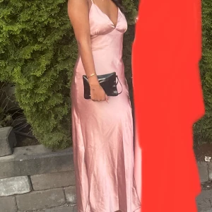 Ljusrosa balklänning - Säljer en ljusrosa balklänning i satin med djup v-ringning och smala axelband. Klänningen har en figurnära passform och en liten slits på vänster sida. På mig som är 179 cm lång är den precis på gränsen för att vara för kort i längden men väldigt fin