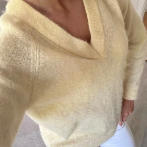 Ljusgul stickad tröja med v-ringning - Supermjuk och fluffig ljusgul stickad tröja med djup v-ringning och långa ärmar. Tröjan har en avslappnad passform och bred ribbad kant vid halsen. Perfekt för dig som gillar en enkel men ändå trendig look.