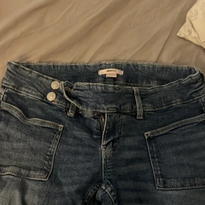Blå slitna jeans från Gina Tricot - Säljer ett par blå jeans från Gina Tricot med coola slitningar på benen och stora framfickor. Jeansen har hög midja, raka ben och dubbla knappar i midjan. Perfekta för en avslappnad och trendig look.