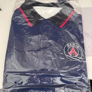 Paris saint-germain-Men’s polo shirt - Aldrig använd.                                                             Pris kan diskuteras , passar xs-m.                           Blå pikétröja från Paris Saint-Germain med klassisk krage i svart och röda detaljer. Tröjan har knappar framtill och stor PSG-logga på bröstet. 